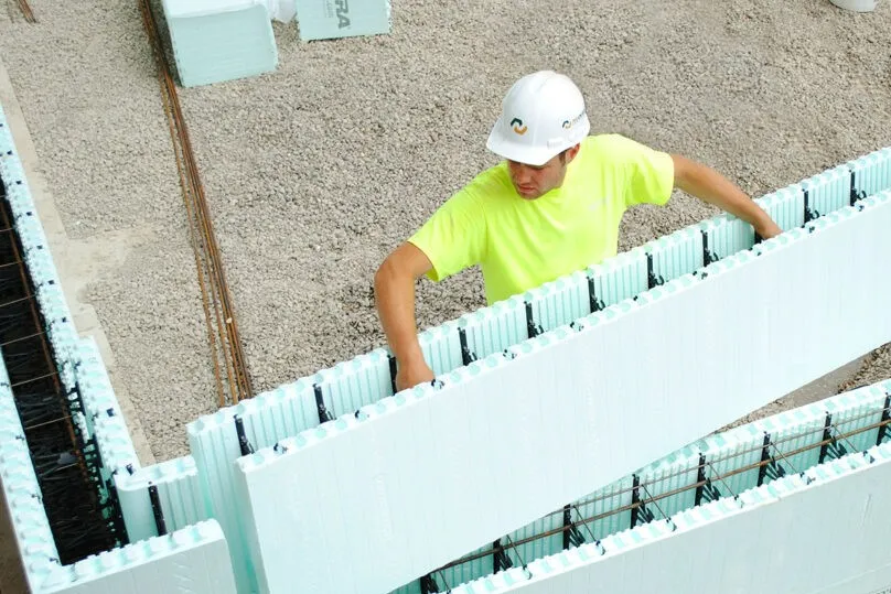 Worker installing ICF wall forms with steel reinforcement positioned inside the concrete cavity.